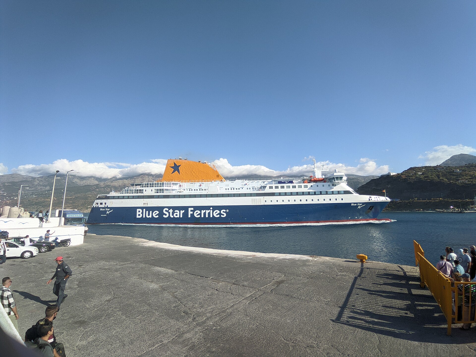 A Blue Star Ferries vessel arriving at a Greek island quay with foot passengers waiting behind a barrier