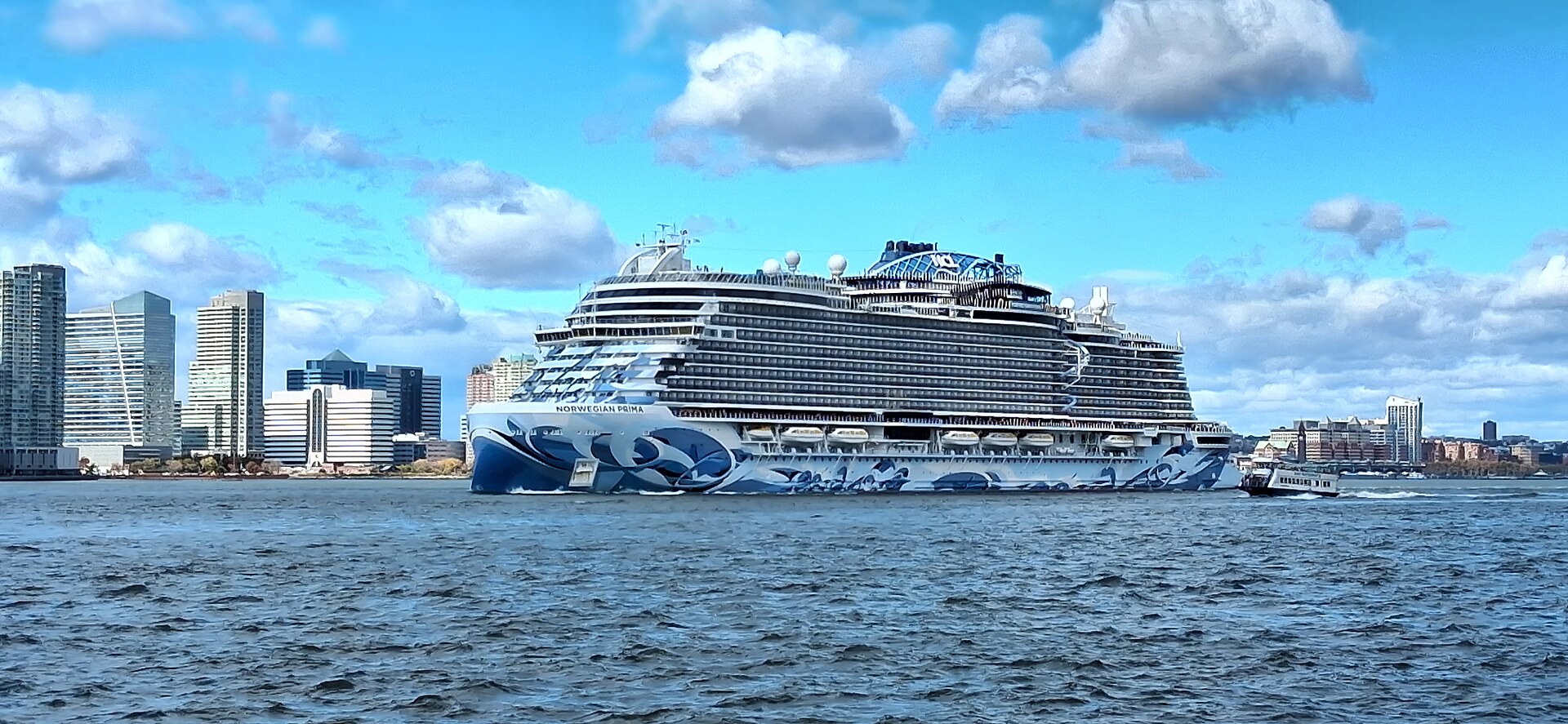 The cruise ship Norwegian Prima under way with a city skyline behind
