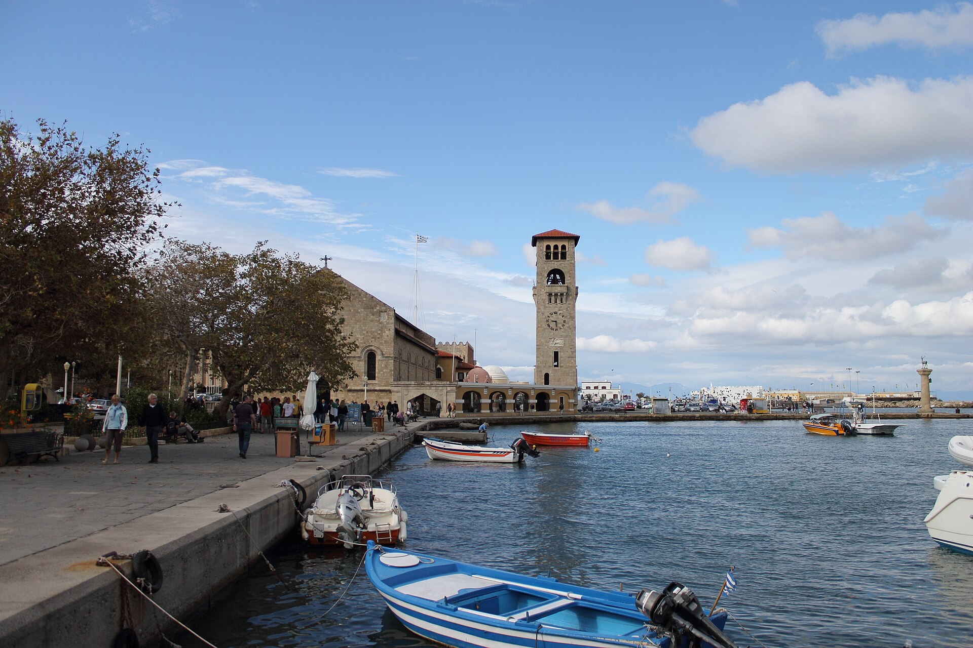 Mandraki Harbour in Rhodes Town in October, with small boats moored and few people on the quay