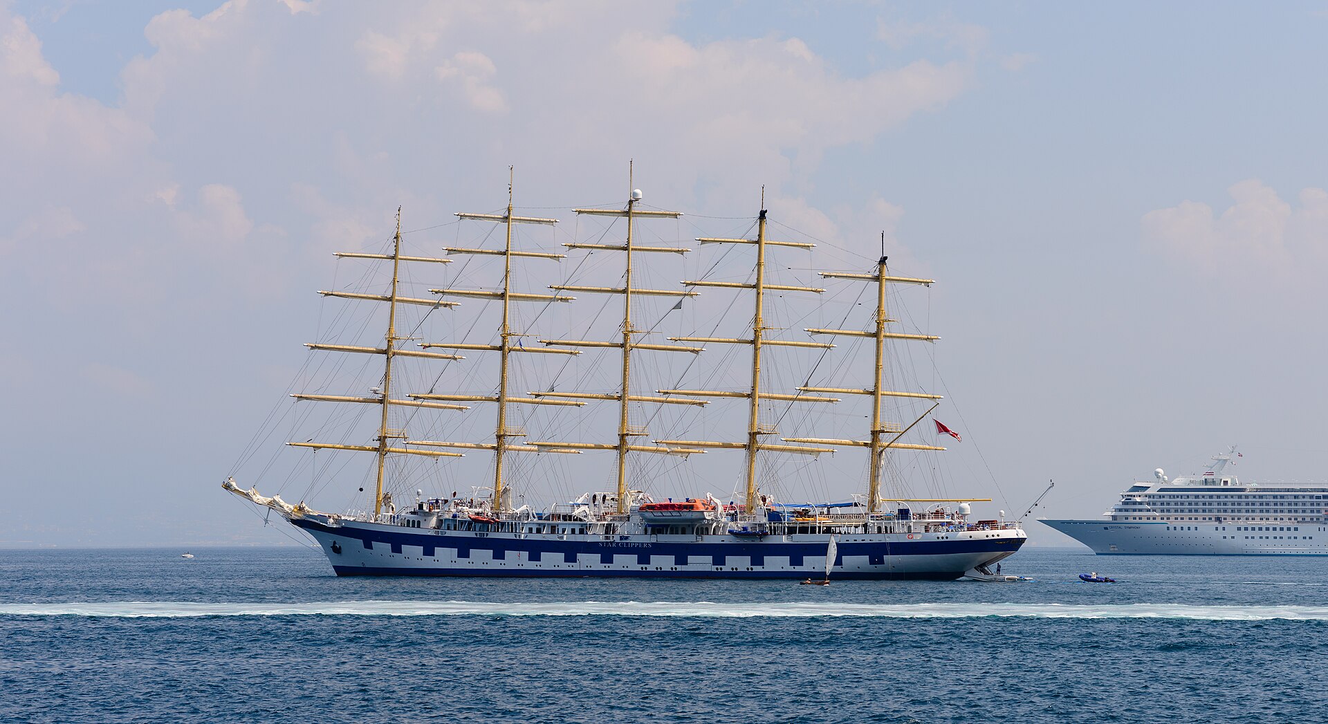 A five-masted Star Clippers sailing ship anchored off the Italian coast beside a much larger conventional cruise ship
